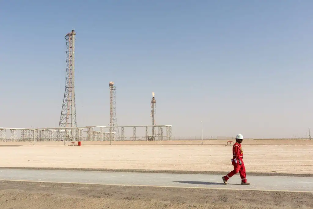 Oil and gas worker walking in Dubai oil field with industrial structures.