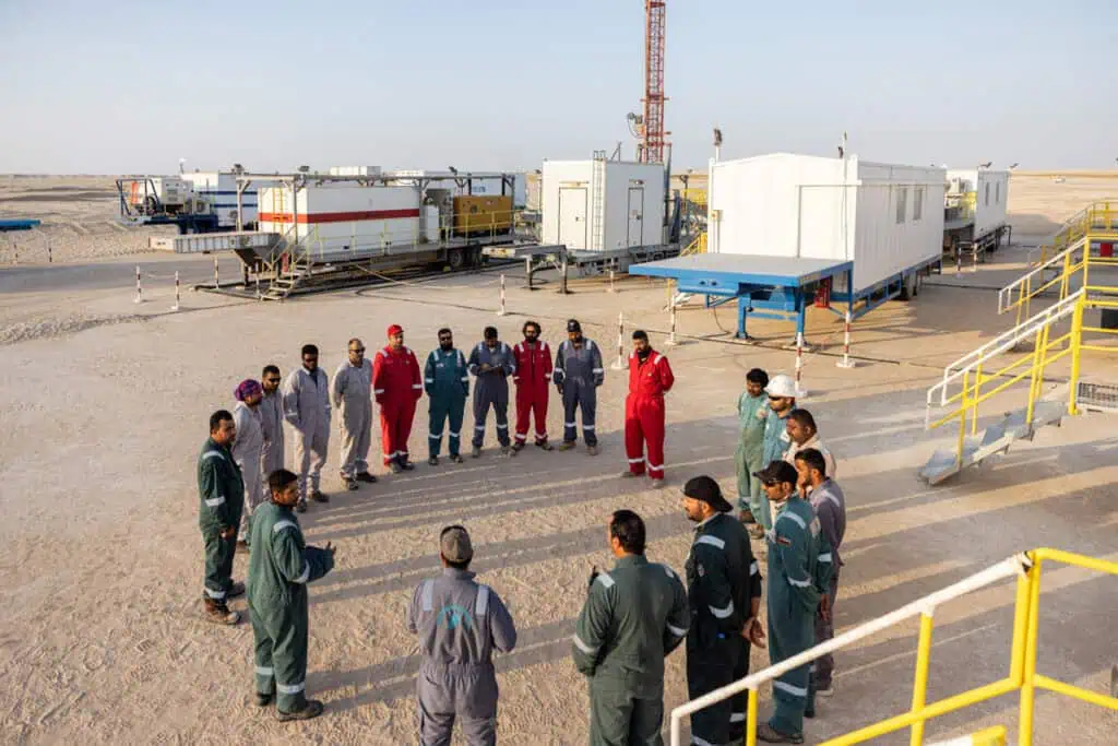 Oil and gas workers and engineers in a desert site during a team briefing.