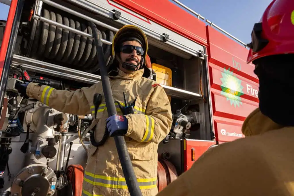 Firefighter holding hose near fire truck in Dubai, emergency response scene.
