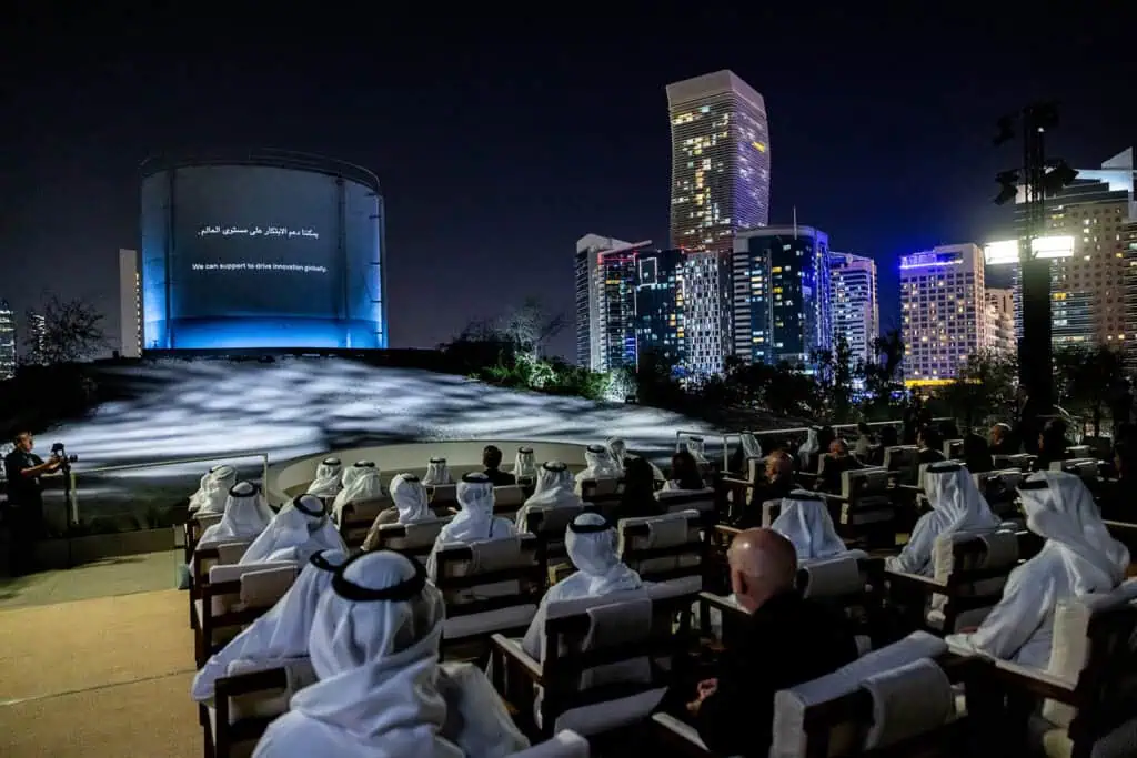 Nighttime corporate event in Dubai with audience and city skyline.